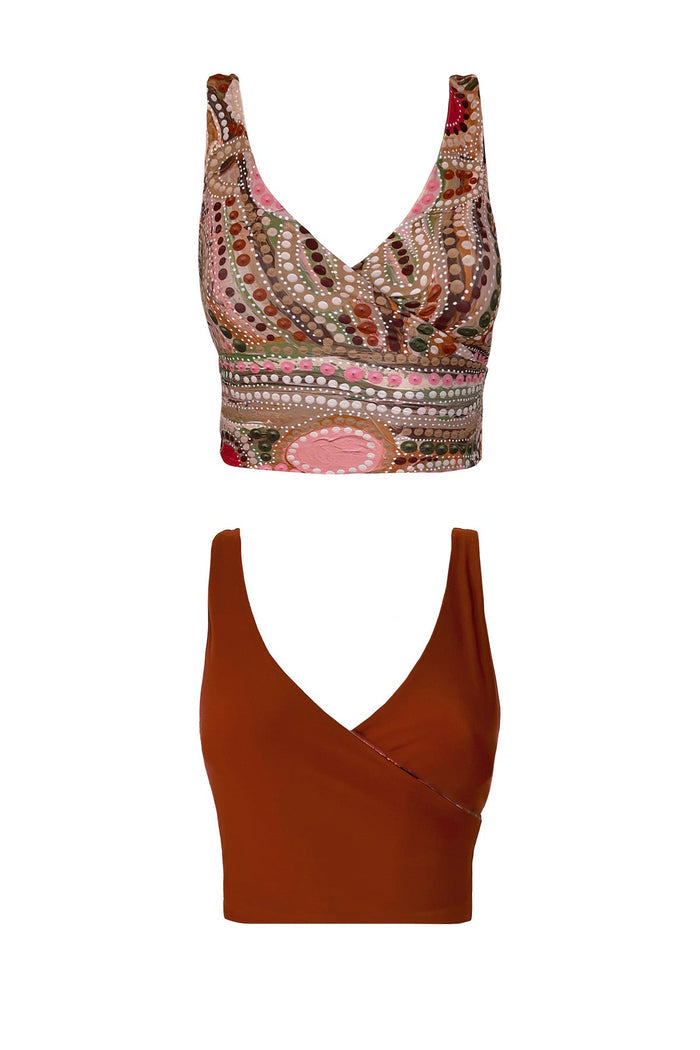 A product image of the reversible Guyulgang bikini top. One side is a solid rust colour and the other features a vibrant hand painted indigenous print featuring khaki, raspberry pink, rust and beige tones.