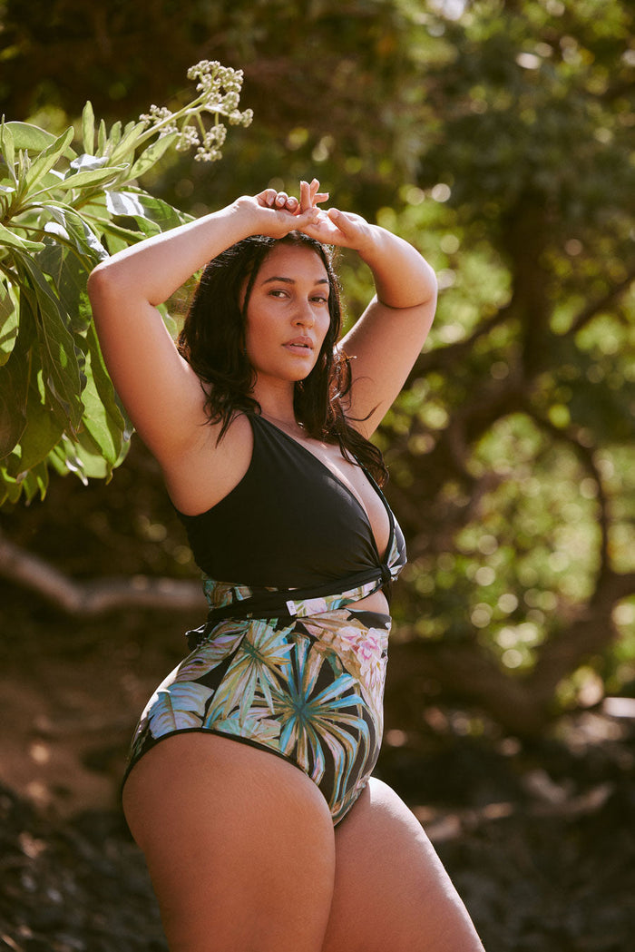 Plus size woman wears shaping black bikini with high waisted tropical print bottoms.