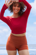 Woman wearing a raspberry coloured long sleeve wrap top with high waisted clay swim shorts.