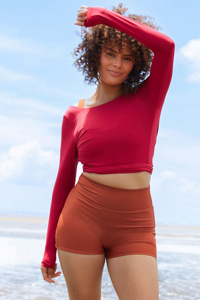 Woman wearing a raspberry coloured long sleeve wrap top with high waisted clay swim shorts.
