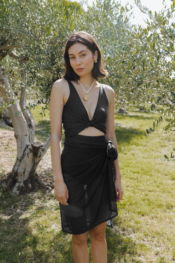 Woman wears black mesh sarong around waist, and black bikini top.