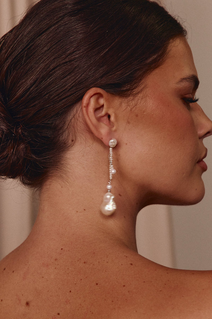 Close-up of a woman wearing pearl earrings with a neutral background